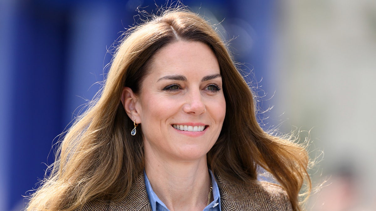 A close-up of Kate Middleton smiling in a brown blazer.