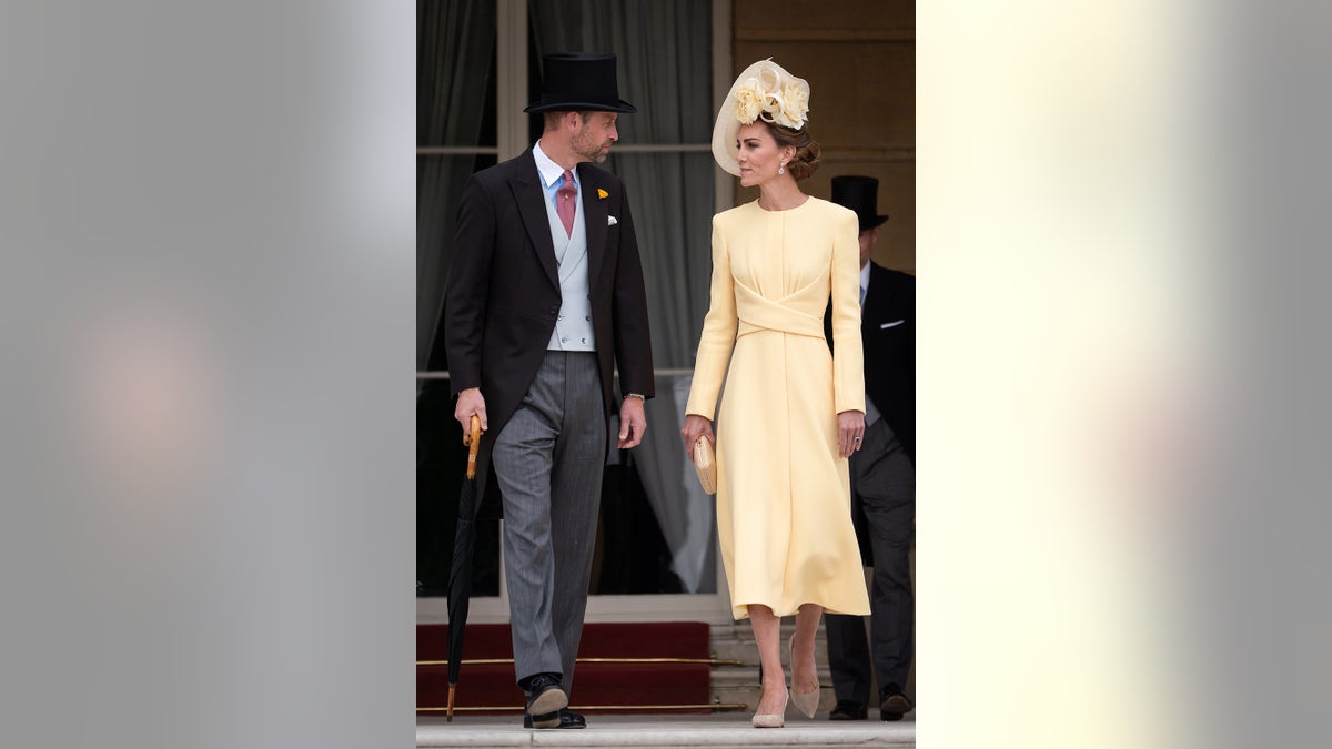 Kate Middleton wearing a butter yellow dress and matching hat walking alongside Prince William in a suit and top hat.