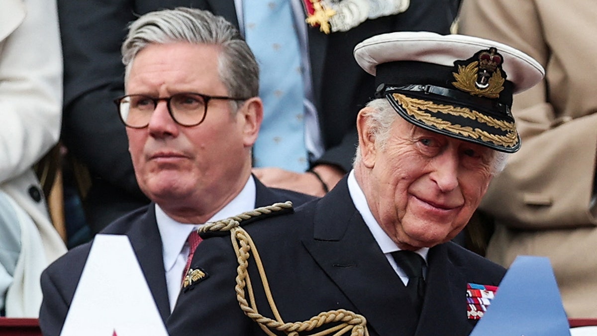 A close=up of King Charles smiling in uniform in front of the U.K. Prime Minister.