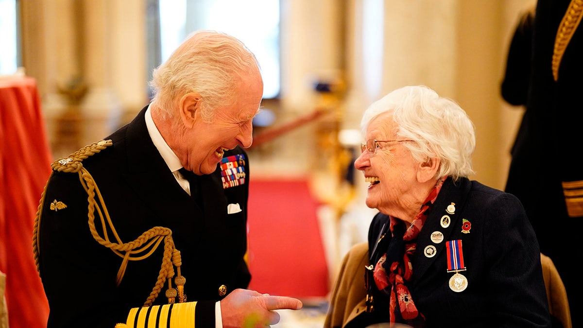 King Charles smiling with an elderly woman inside the palace.
