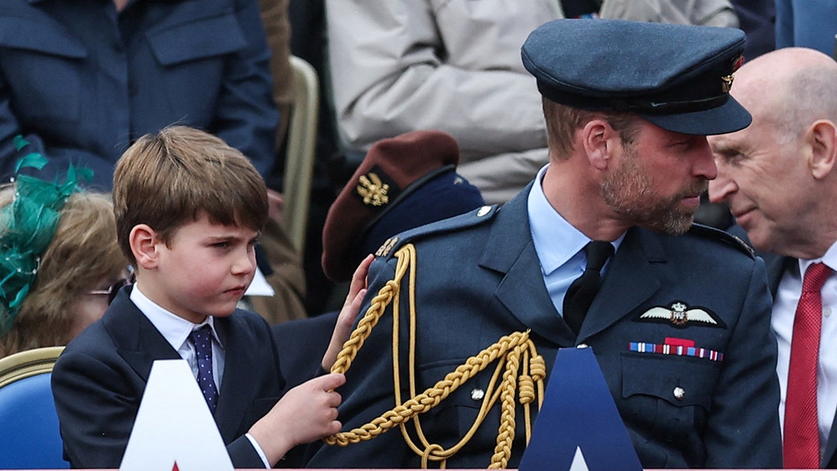 Prince Louis clutching onto his father Prince William's tassels as they sit together.