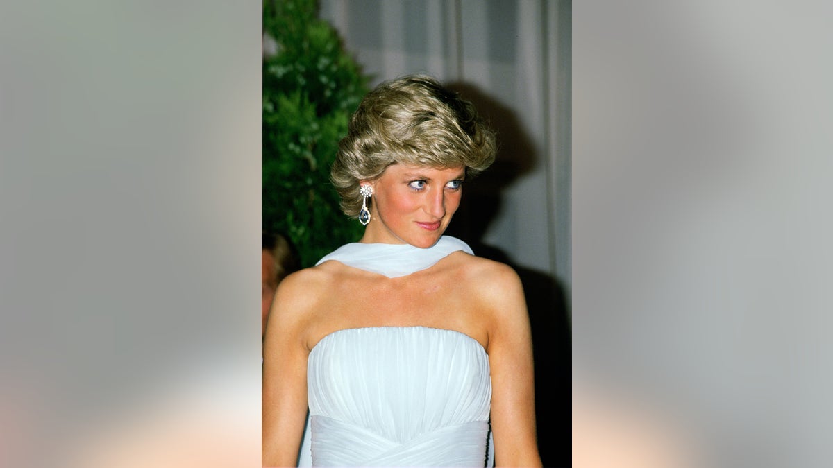 Princess Diana wearing a shoulder-baring light blue dress with a matching scarf smirking.