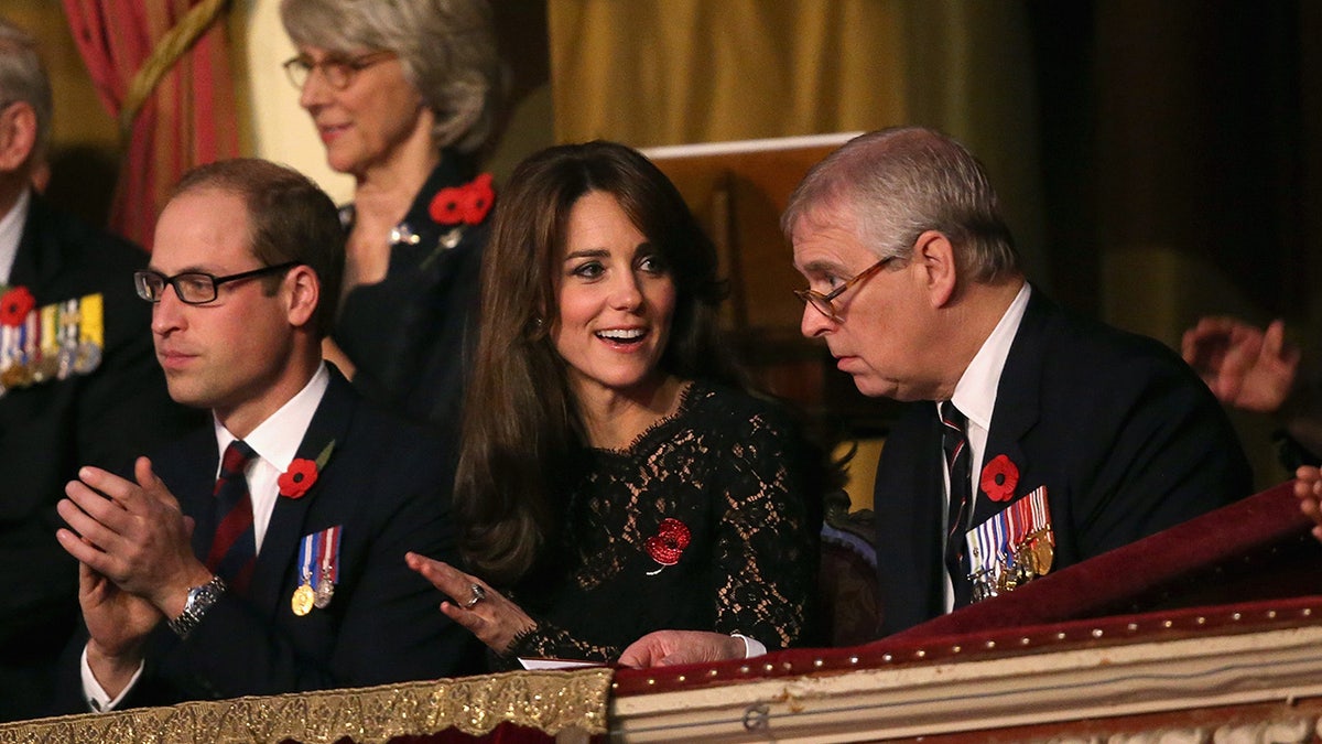 Prince William sitting with glasses next to Kate Middleton who looks at Prince Andrew, also wearing glasses.