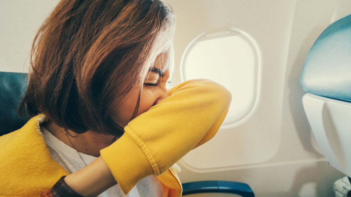 female airplane passenger sneezes into her elbow. First signs of corona virus and covid-19 infection during air transportation