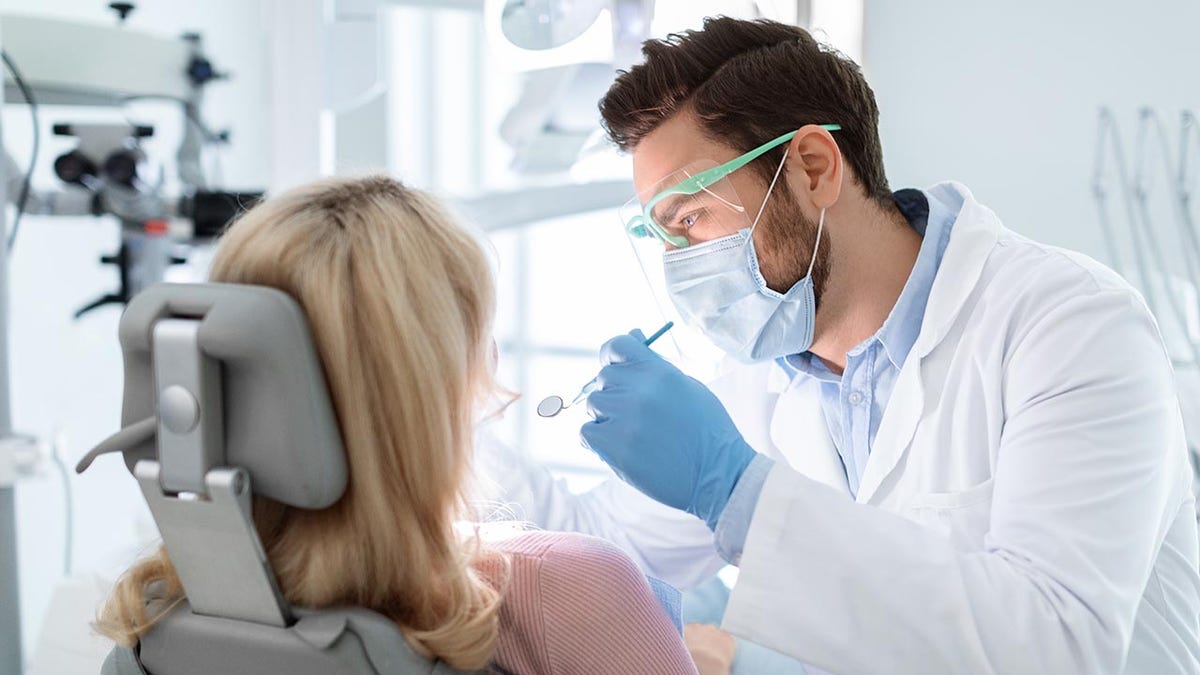 Dentist treats woman in dental chair.