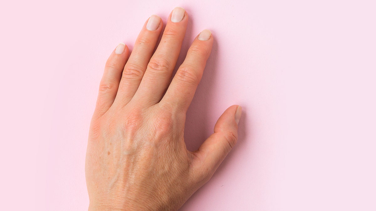 Image of a left hand up close laying flat palm down on a pink background. The nails are manicured and painted light pink.