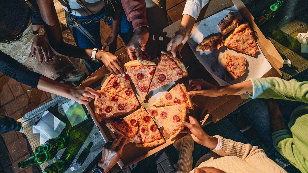 Pizza party, a bunch of hands drawback slices from a pizza oculus successful a bird's oculus view