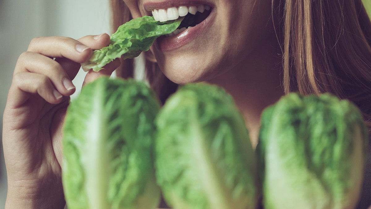 Close-up shot of a woman chewing on some romaine lettuce. We only see her mouth. She is smiling.