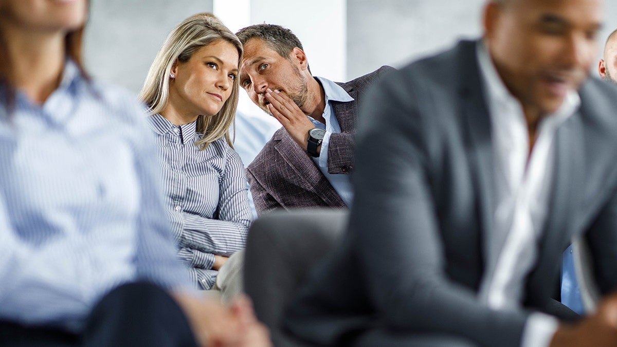 businesswoman listening to her colleague tell her a secret in a meeting