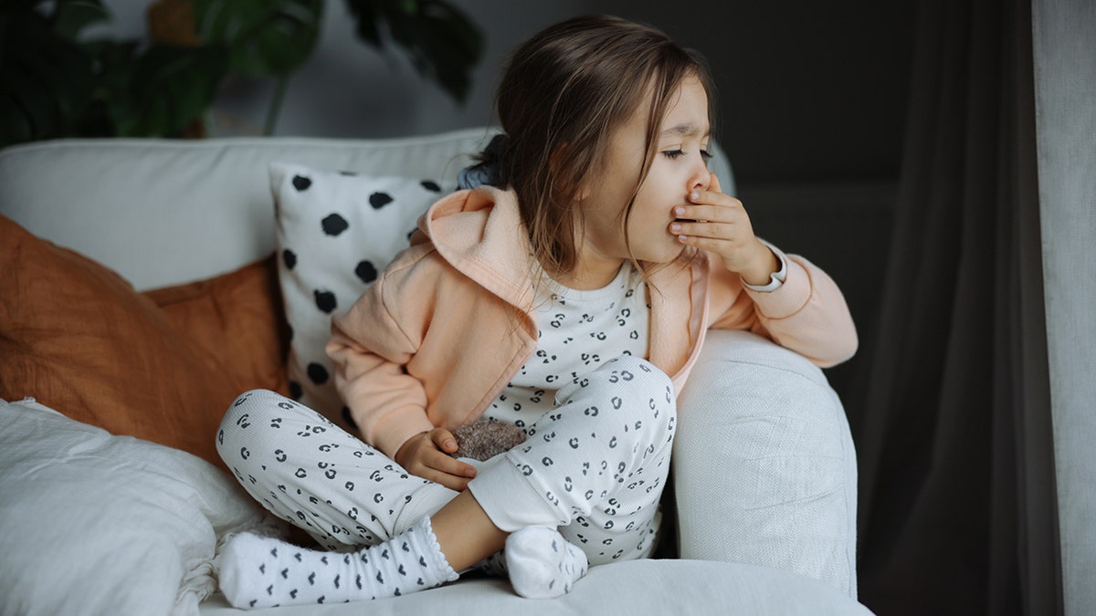 little girl covers her mouth while she coughs