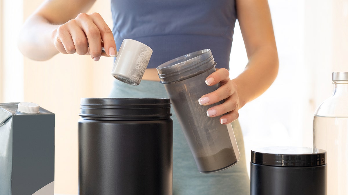 Close shot of two hands preparing some sort of protein shake in a grey container.