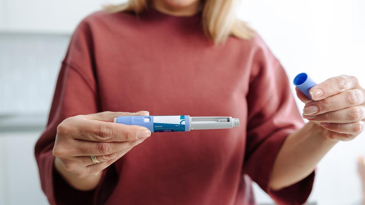 A person holding and preparing a medical injection pen, demonstrating its usage during a healthcare routine.