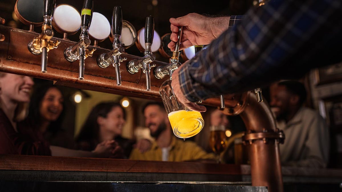 Bartender pulling a pint of beer from a tap for friends in a lively cozy traditional pub