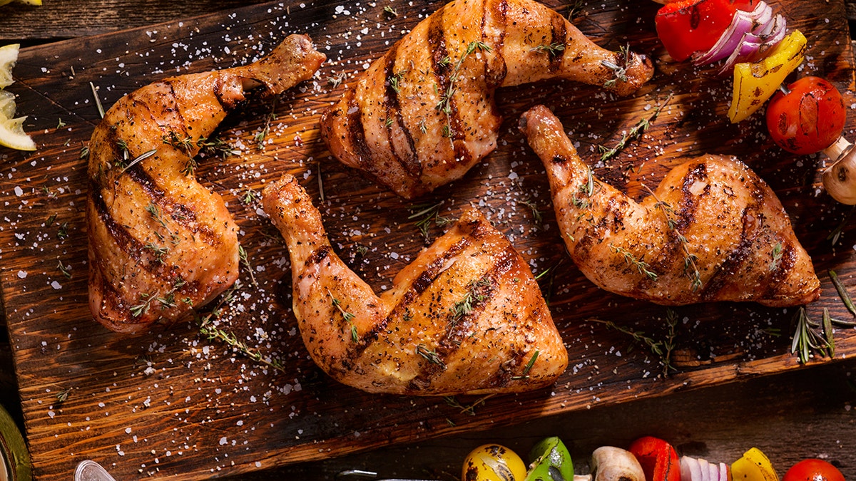 Quatro pedaços de frango grelhado são mostrados em uma tábua de madeira.
