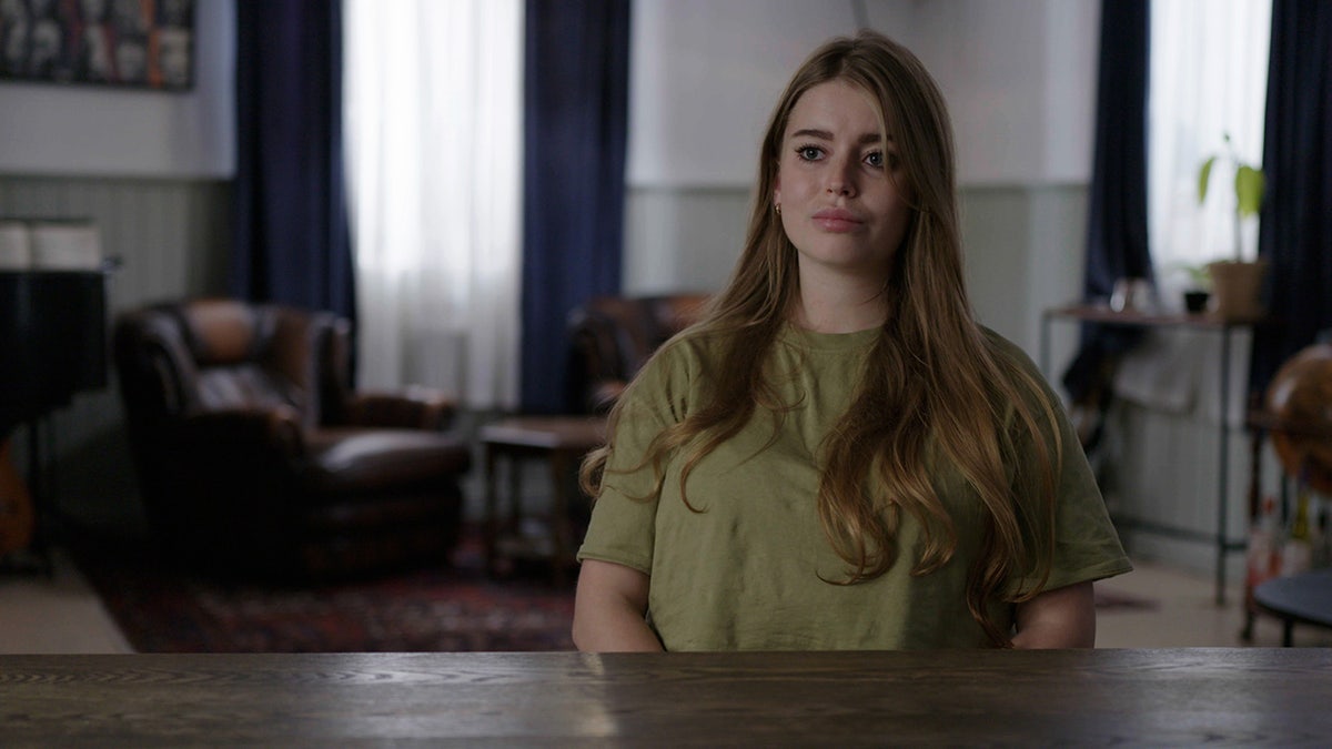Jamie-Lee Arrow sitting in front of a desk wearing an olive shirt.