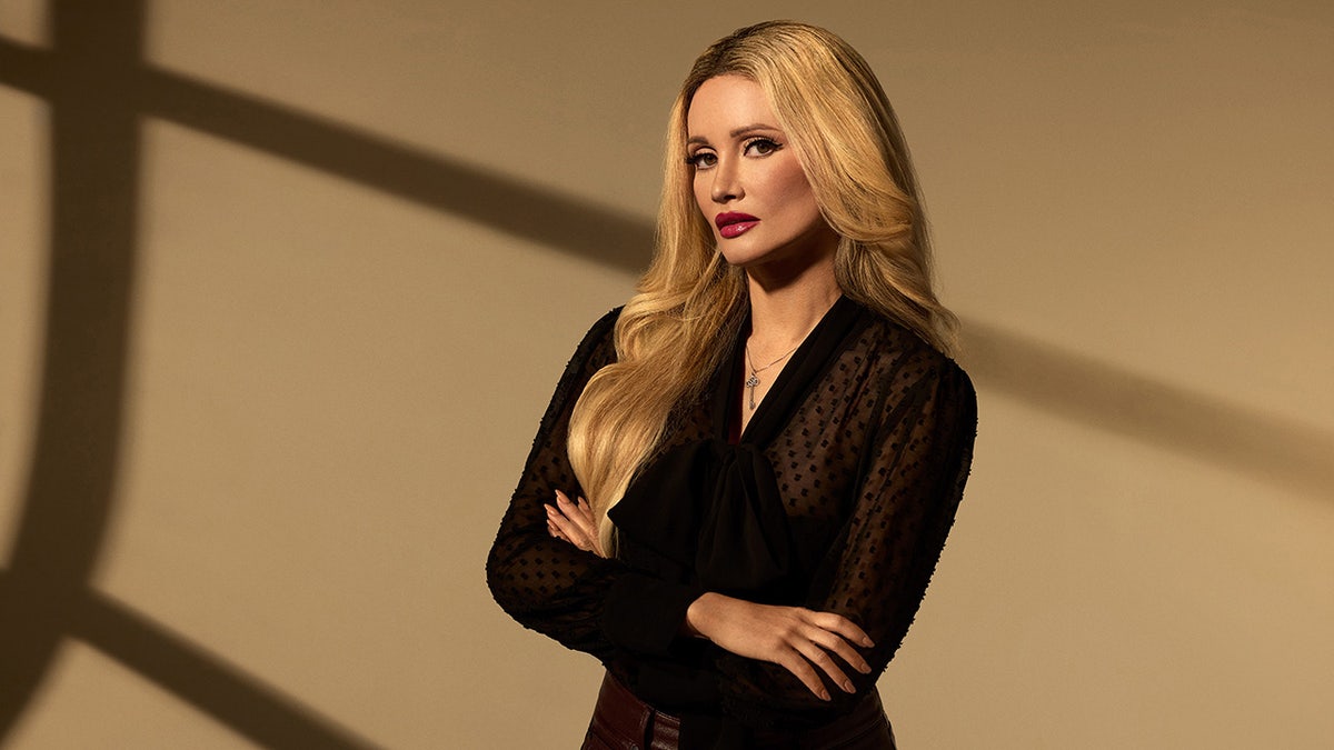 Holly Madison with her arms crossed wearing a sheer black top.
