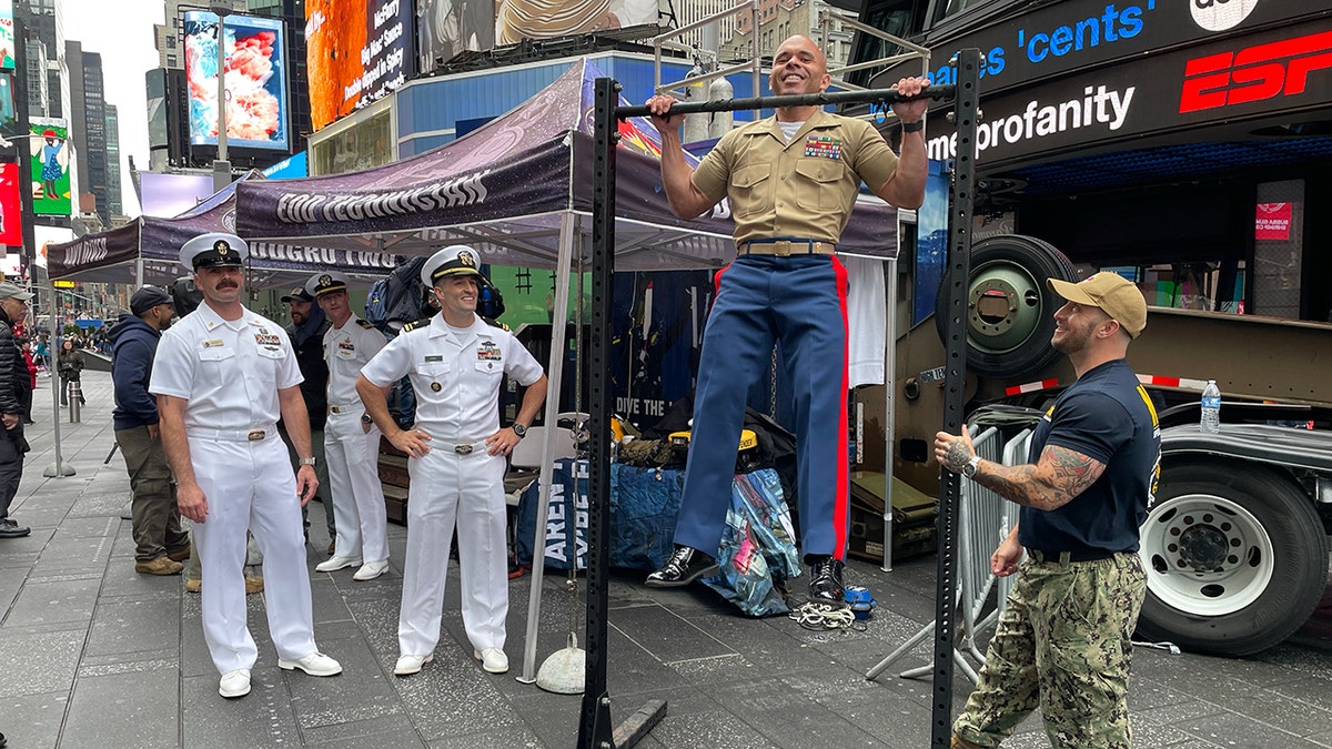 One of the military members smiling while performing a chin-up on the bar outside of the Navy display setup.