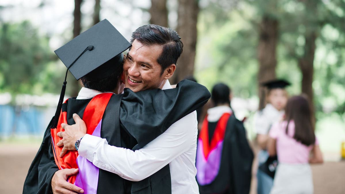Portrait of a happy student wearing graduation gown hugging a parent.