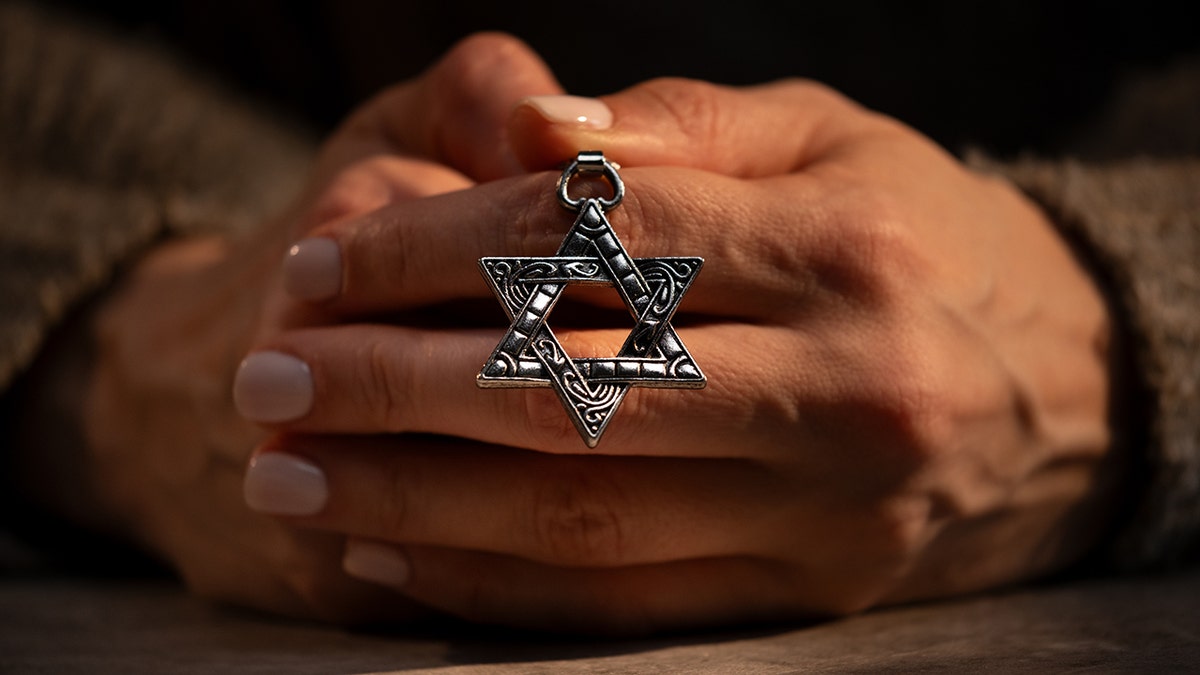Woman holding necklace with Star of David, nails painted, zoomed into hands