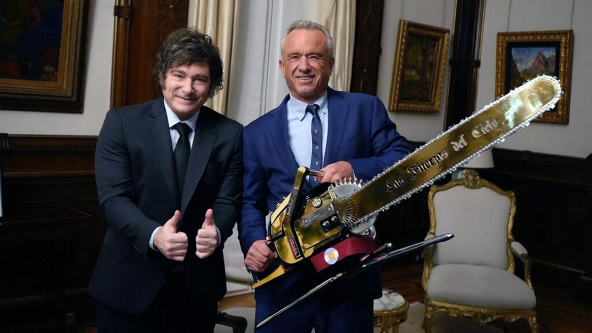 Robert F. Kennedy Jr. holds a gold chainsaw next to Argentine President Javier Milei, both smiling, inside the Casa Rosada.