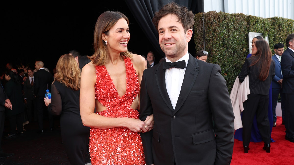 Mandy Moore wears a red dress and walks a red carpet with her husband