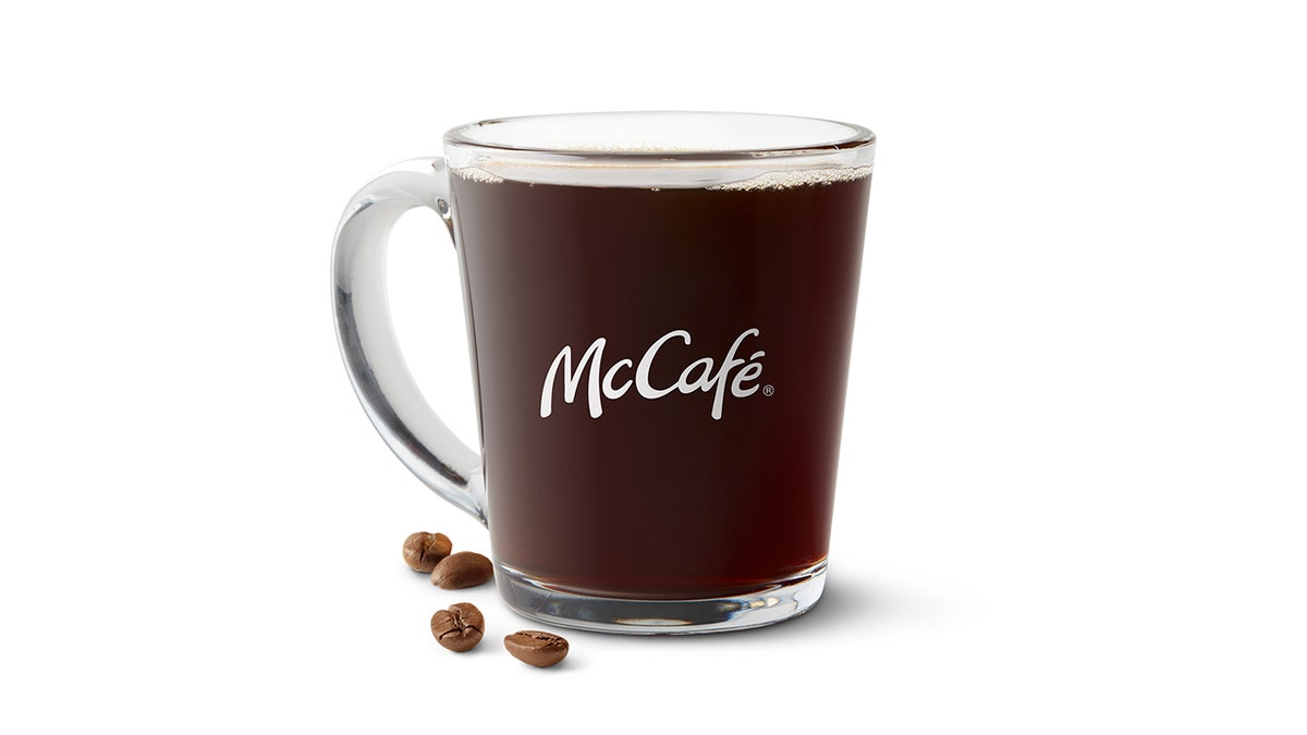 A cup of McCafé coffee from McDonald's is presented on a white background with four coffee beans next to it.