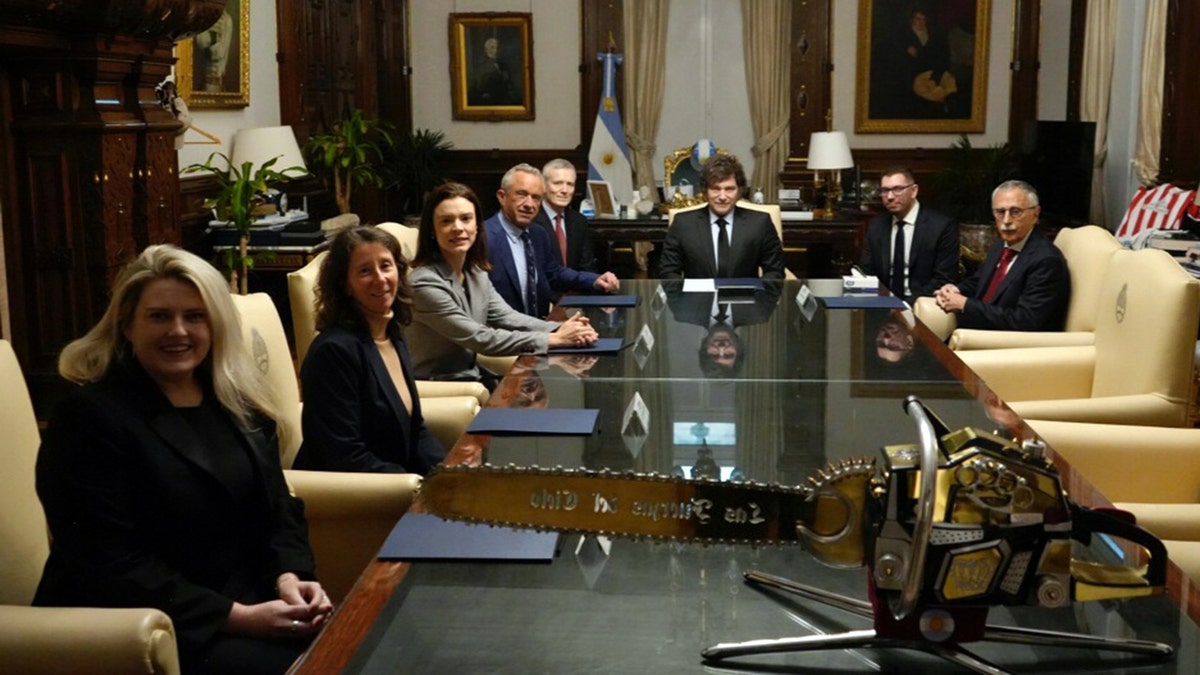 Kennedy and Milei sit with officials around a conference table inside Casa Rosada, with a gold chainsaw displayed in the foreground.
