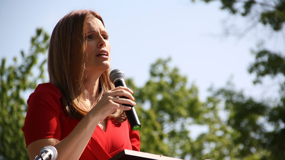 Justice Allison Riggs wears a red shirt while speaking into a microphone