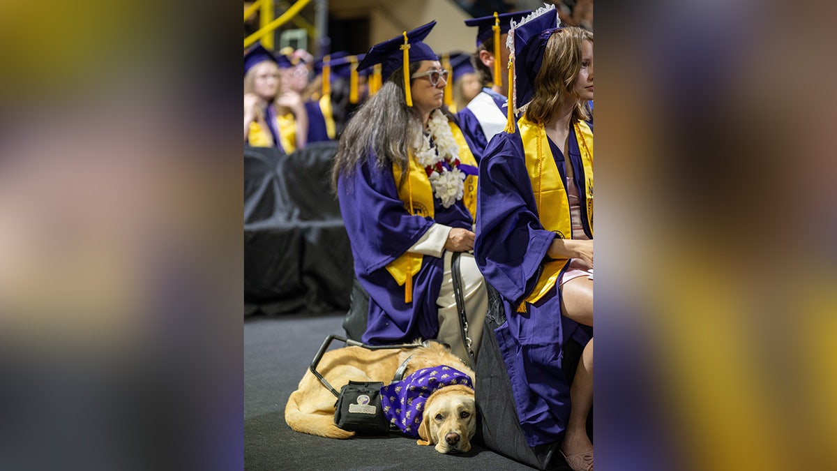 A blind woman in graduation robes raises her fist in celebration during her commencement ceremony.
