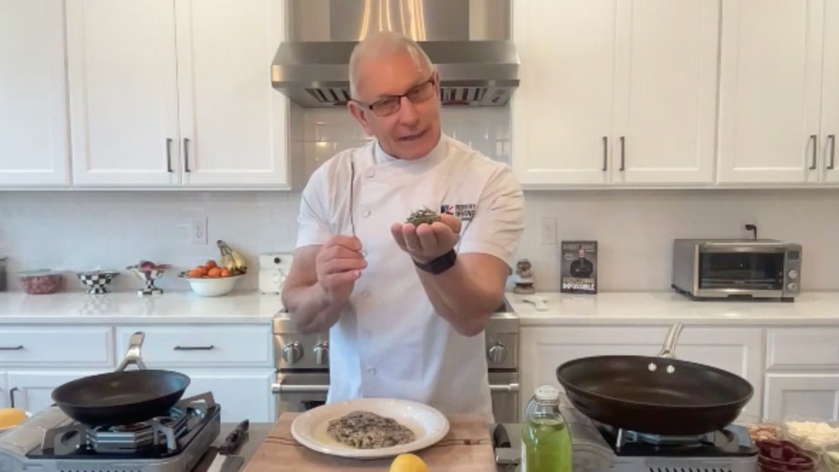 Chef Robert Irvine holds rosemary in his hand and the stem in the other while cooking in his kitchen.