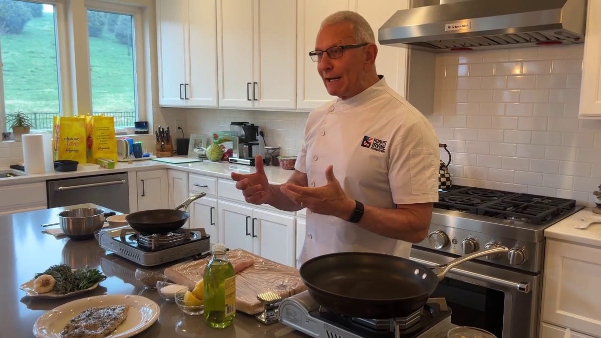 Robert Irvine speaks while preparing a meal in his kitchen.