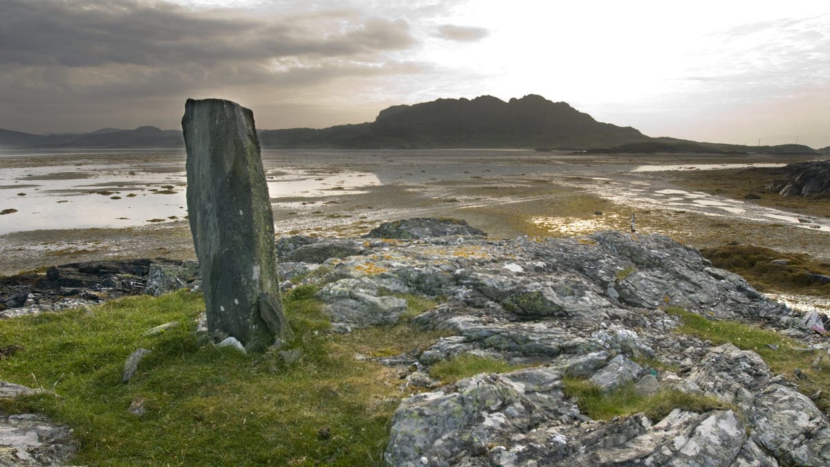 Standing stone on Colonsay, the Hebrides. Mountain can be seen in the distance on a cloudy shore