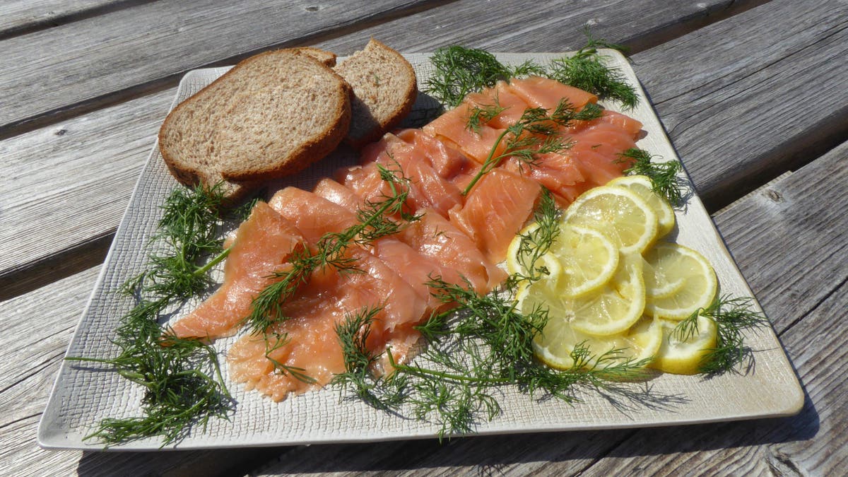 Salmon from the Colonsay Smokery, Colonsay, features lemon, dill, and two slices of toast plated artistically on a large plate atop a wooden table