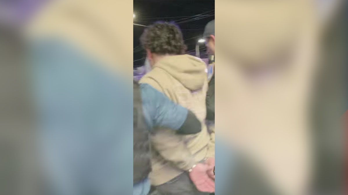 man whose hands are cuffed at his back escorted by police