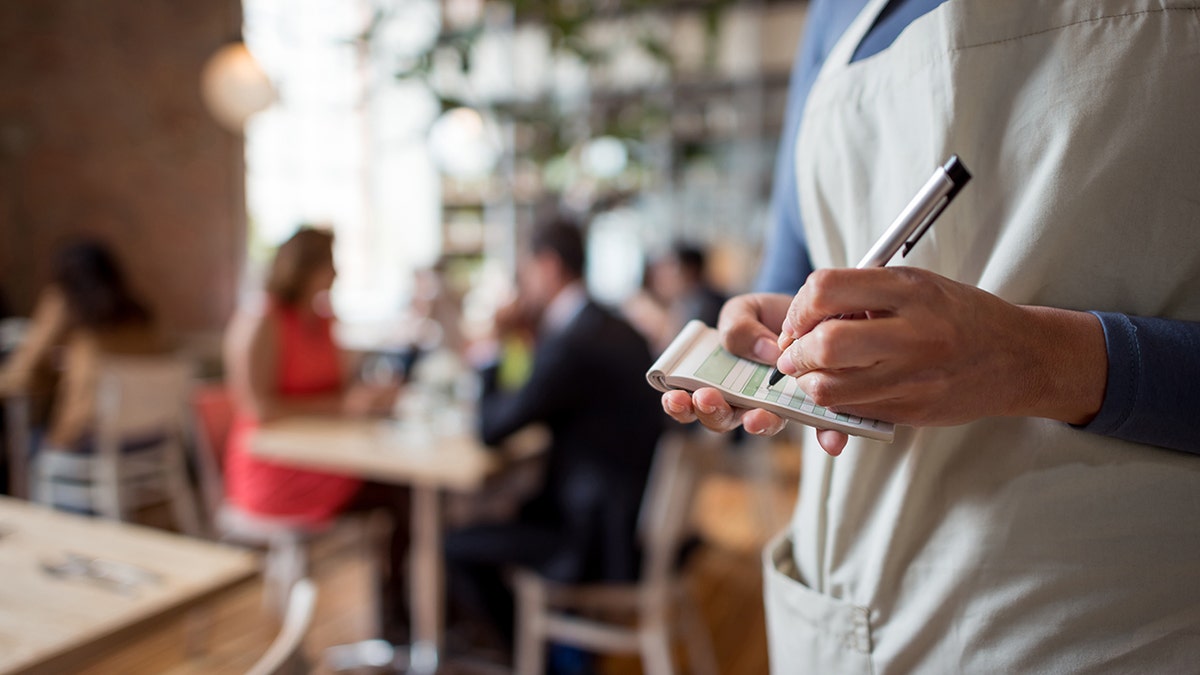 A restaurant server writes down an order with a pen.