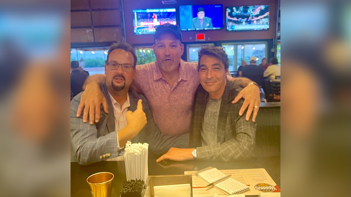 three men hugging at sports bar for photo