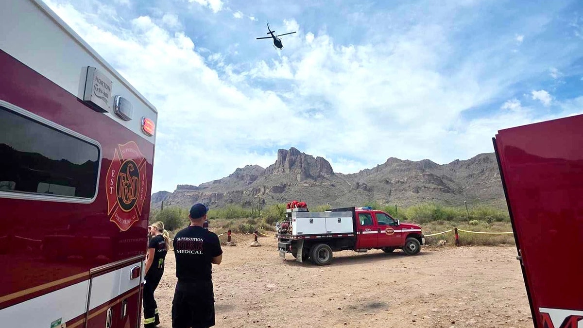 Superstition Fire and Medical responders standing near emergency vehicles as helicopter flies over mountains