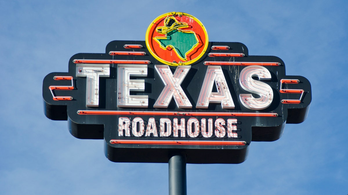 A Texas Roadhouse sign is shown in front of a blue sky.