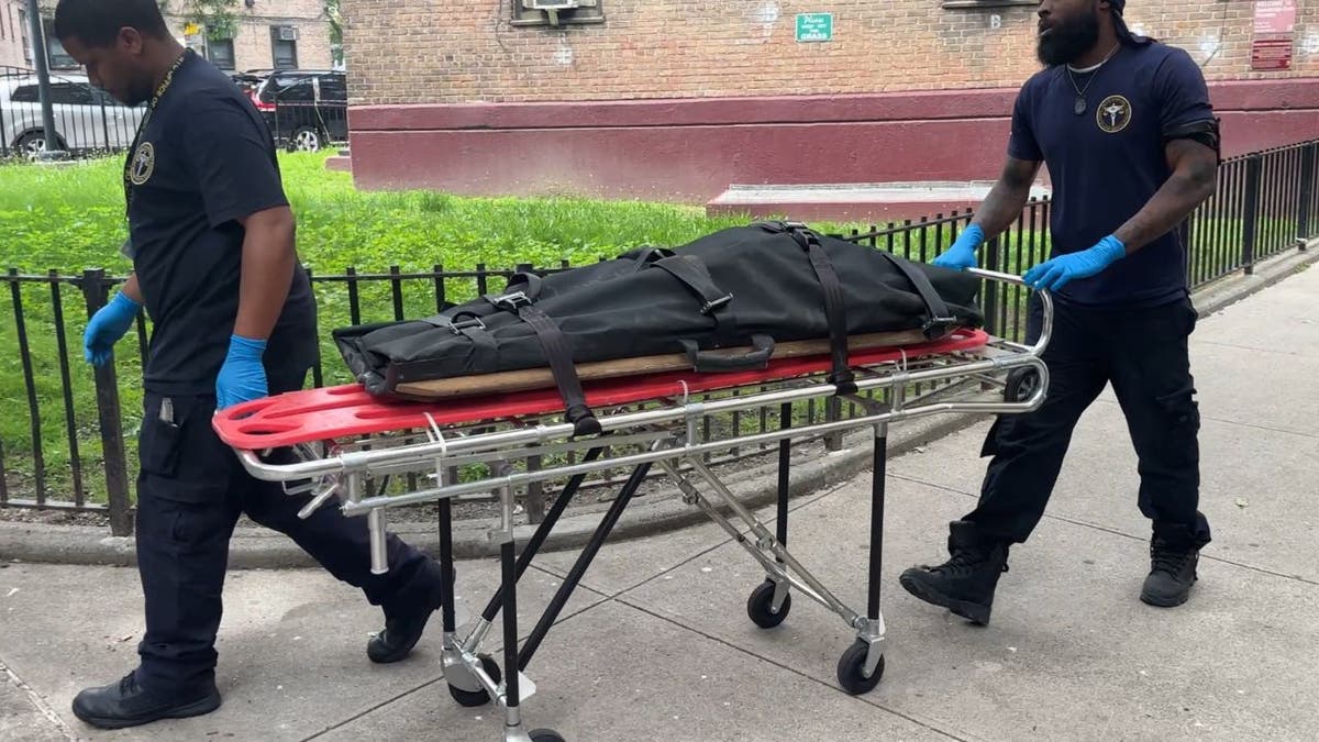 Two men with the Office of the Chief Medical Examiner wheel a gurney out of an apartment building in Queens, New York City.