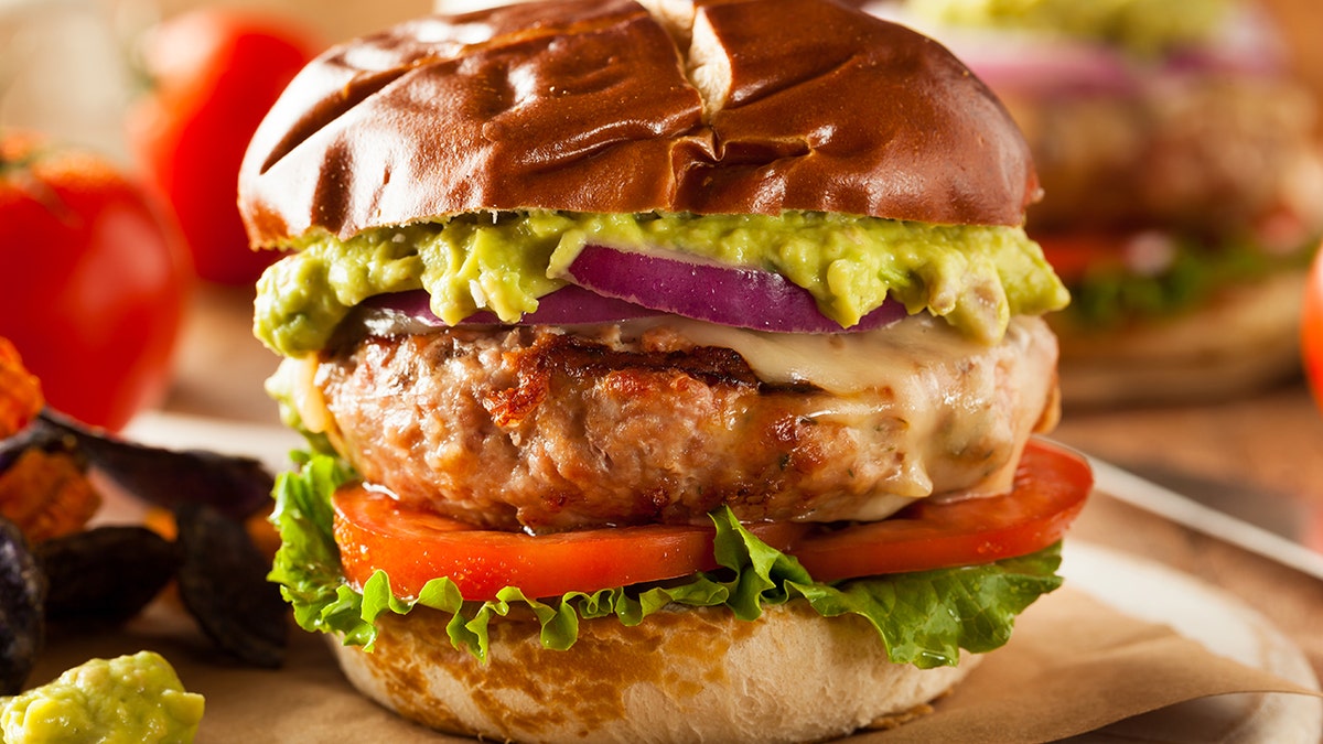A turkey burger with tomatoes, onions and guacamole is shown.