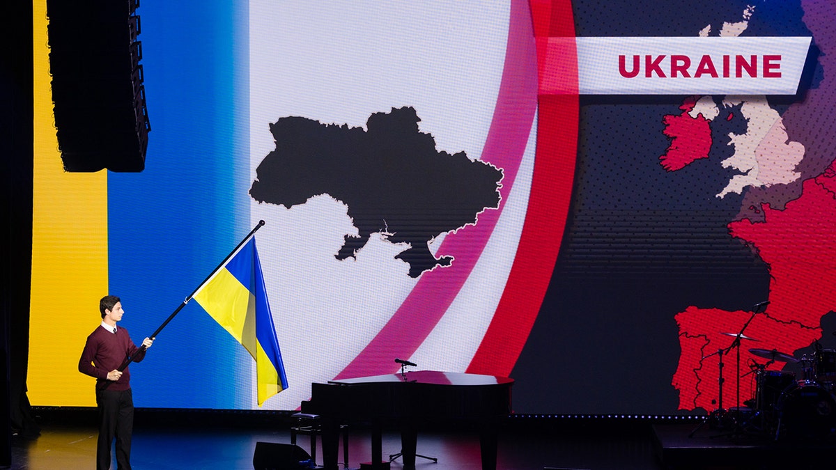A man holds the Ukrainian flag on stage in front of a large digital map of Europe during the European Congress on Evangelism in Berlin