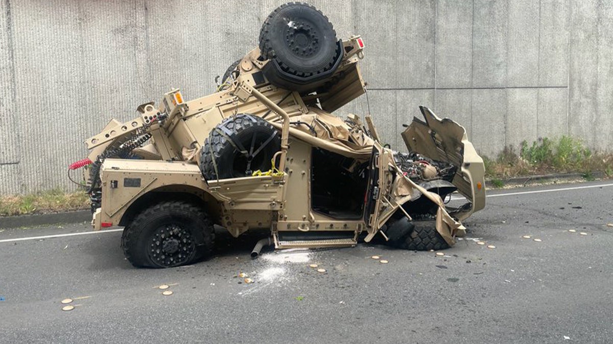 Wrecked military Humvee and trailer on a city street below an overpass