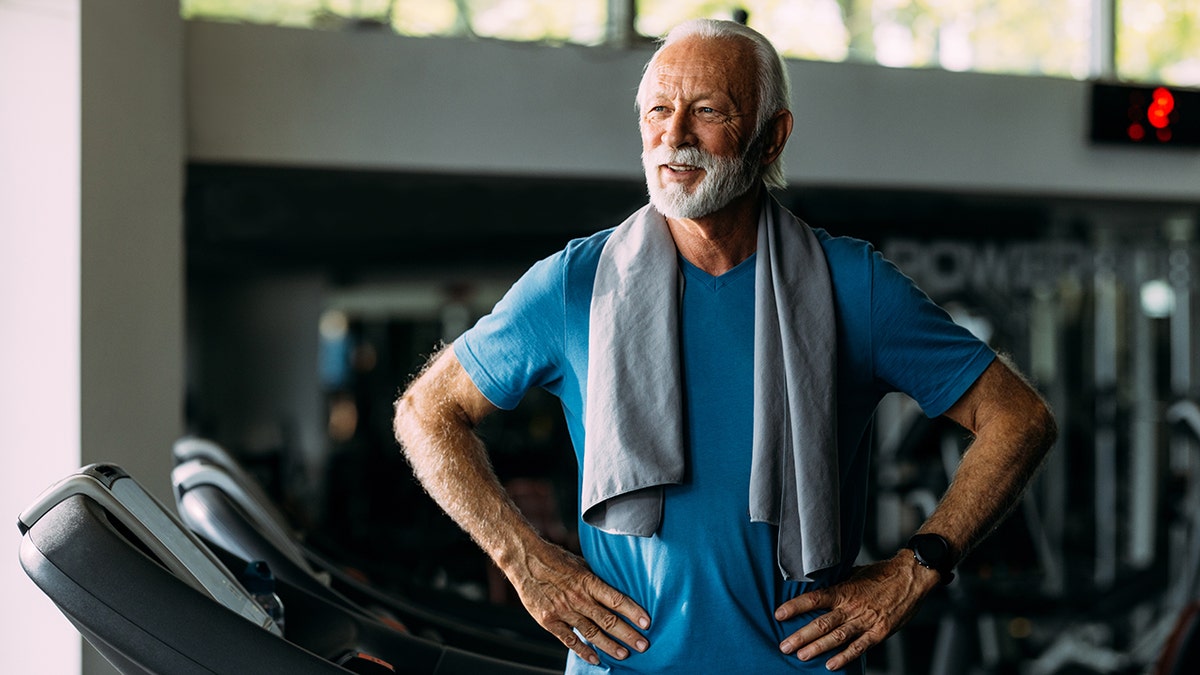 Older man standing on treadmill in gym, looking confident and fit with a towel around his neck: used in piece about vitamin d being able to protect telomeres and support longer living