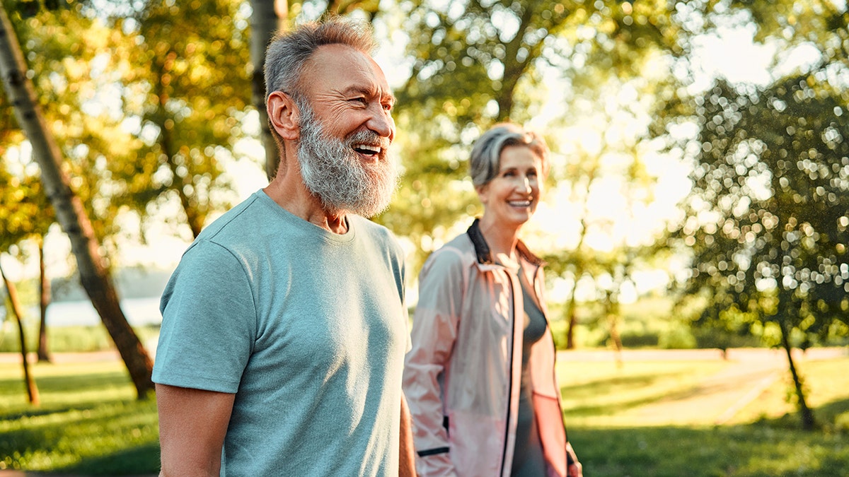 Active hobby on retirement. Grey haired caucasian man with beautiful wife strolling at summer park and smiling cheerfully. Fitness retired couple in sport attire taking break after morning run: used in piece about vitamin d being able to protect telomeres and support longer living