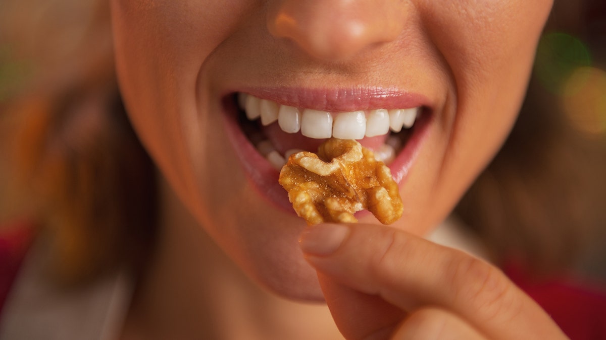 A woman who eats nuts, her lips are shown only while smiling and carrying walnuts until her mouth.