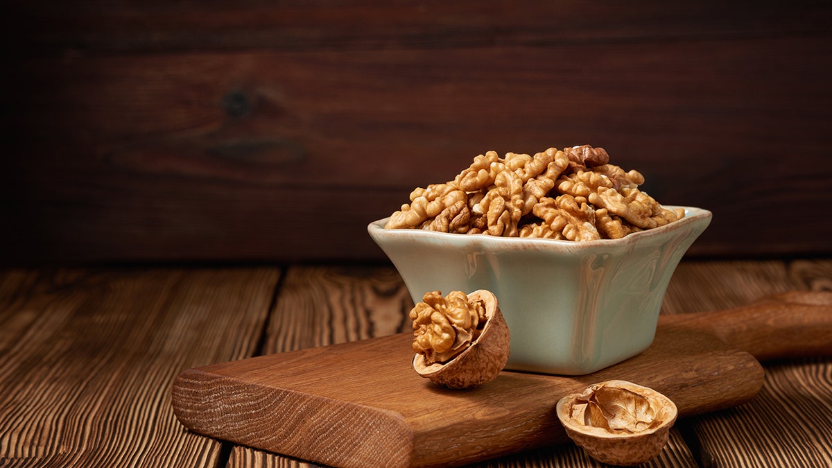 A bowl of walnuts sits on a beautifully lit wood cutting board, all on a wooden table. Close snapshot.