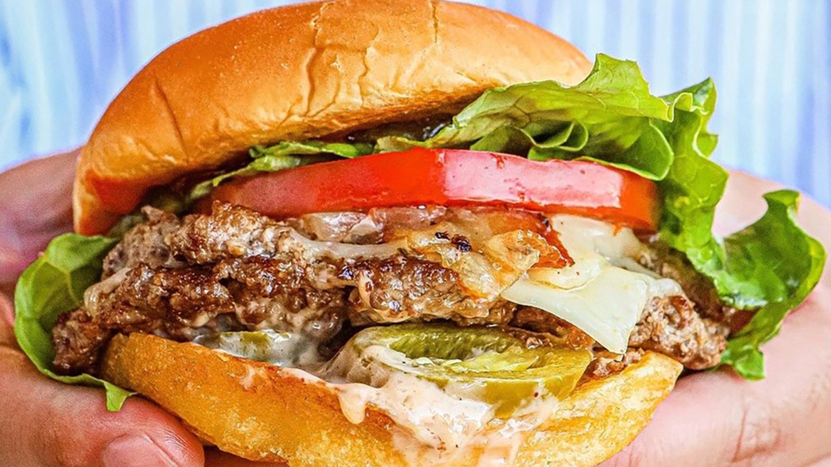 Hands hold a classic burger from Wayback Burgers.