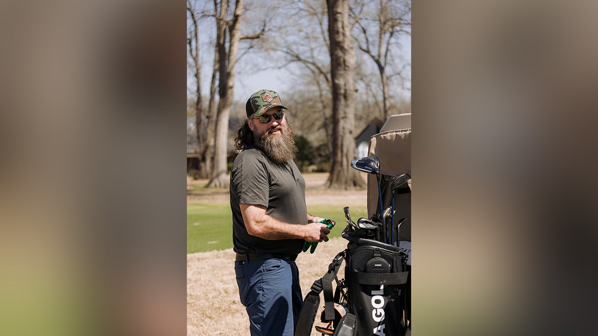 Willie Robertson standing next to golf clubs.