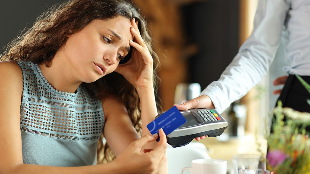 A woman looks worried as she holds a credit card in her hand to pay the bill at a restaurant.