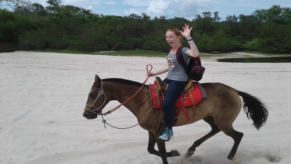 Terrilyn Griffiths riding a horse and smiling pre-injury. The woman is sitting atop a horse outside while the horse gallops.